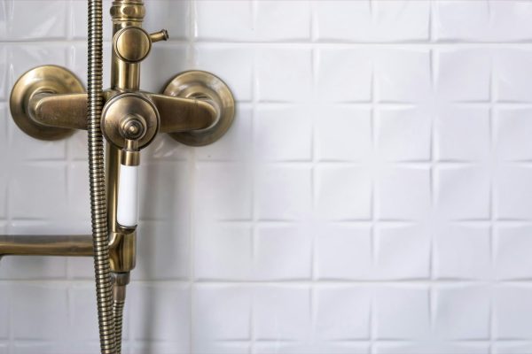 Retro shower bath hand bronze faucet close up, white tile wall background, bathroom interior